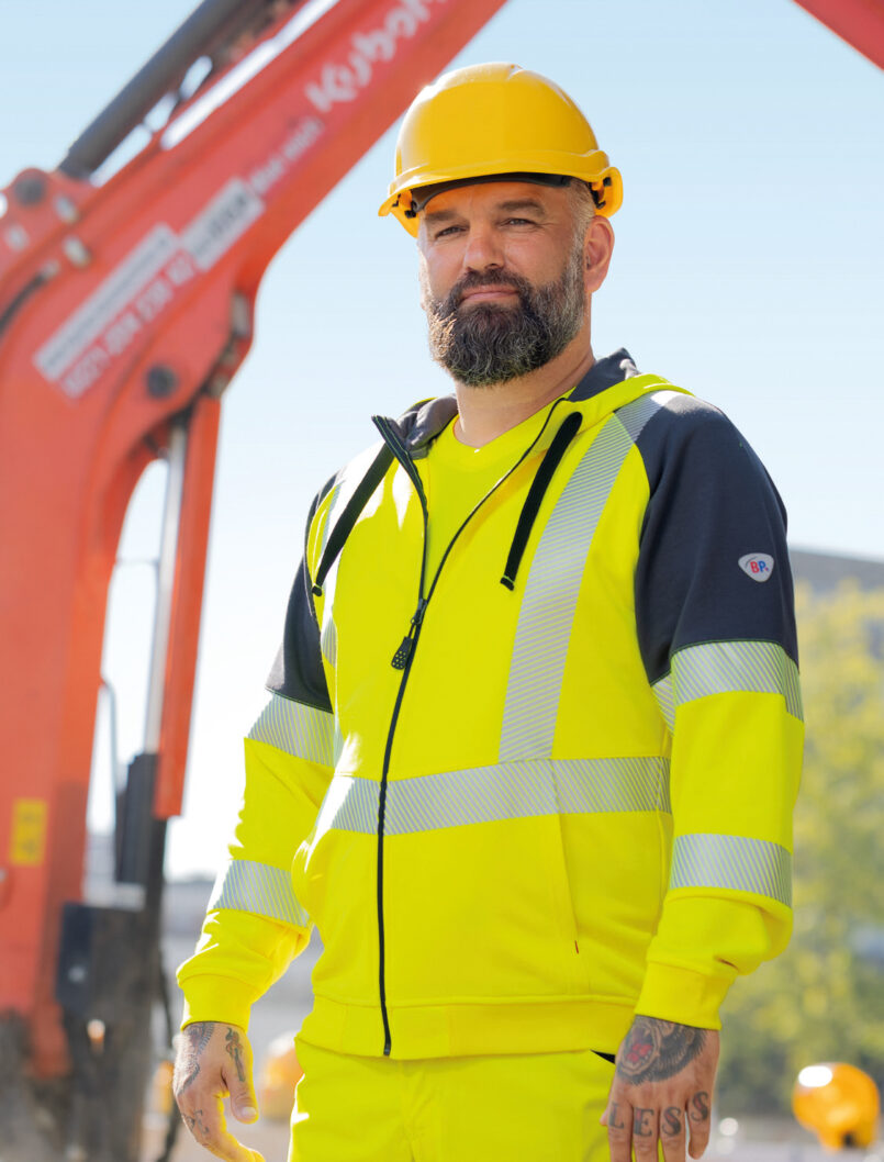 Ein Mitarbeiter trägt Warnschutzkleidung und Helm auf einer Baustelle.